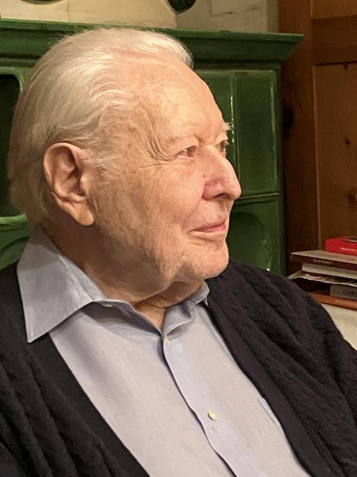 Ein Herr im Profil vor einem grünen Kachelofen sitzend