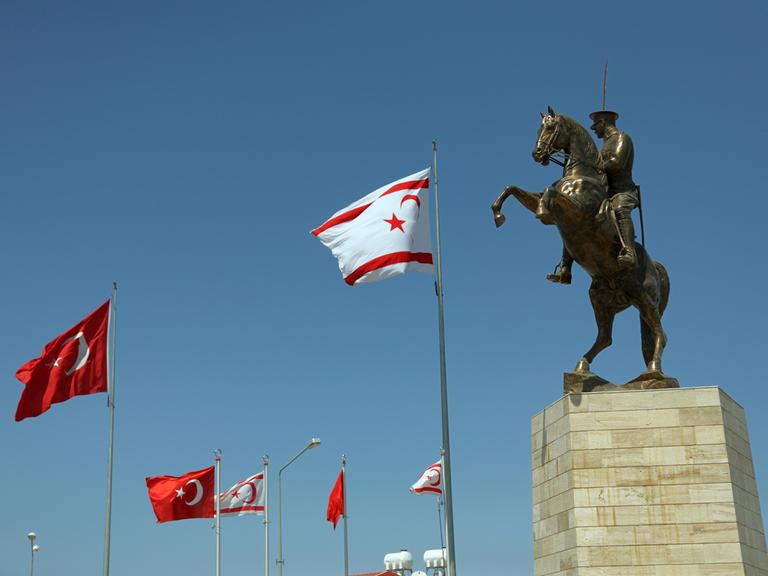 Statue des türkischen Staatsgründers Atatürk auf einem Pferd. Daneben sind türkisch und nordzyprische Nationalflaggen zu sehen.