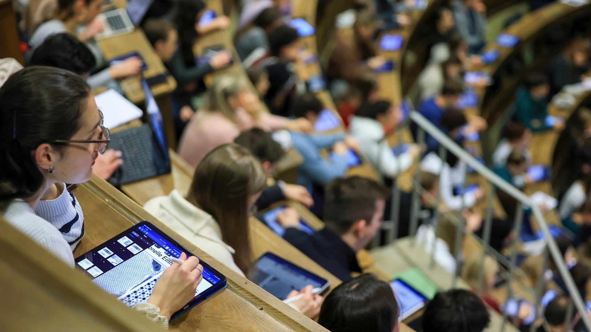 Medizinstudenten sitzen im Hörsaal Anatomie in einer Vorlesung. Im Vordergrund eine junge Frau mit I-Pad. 