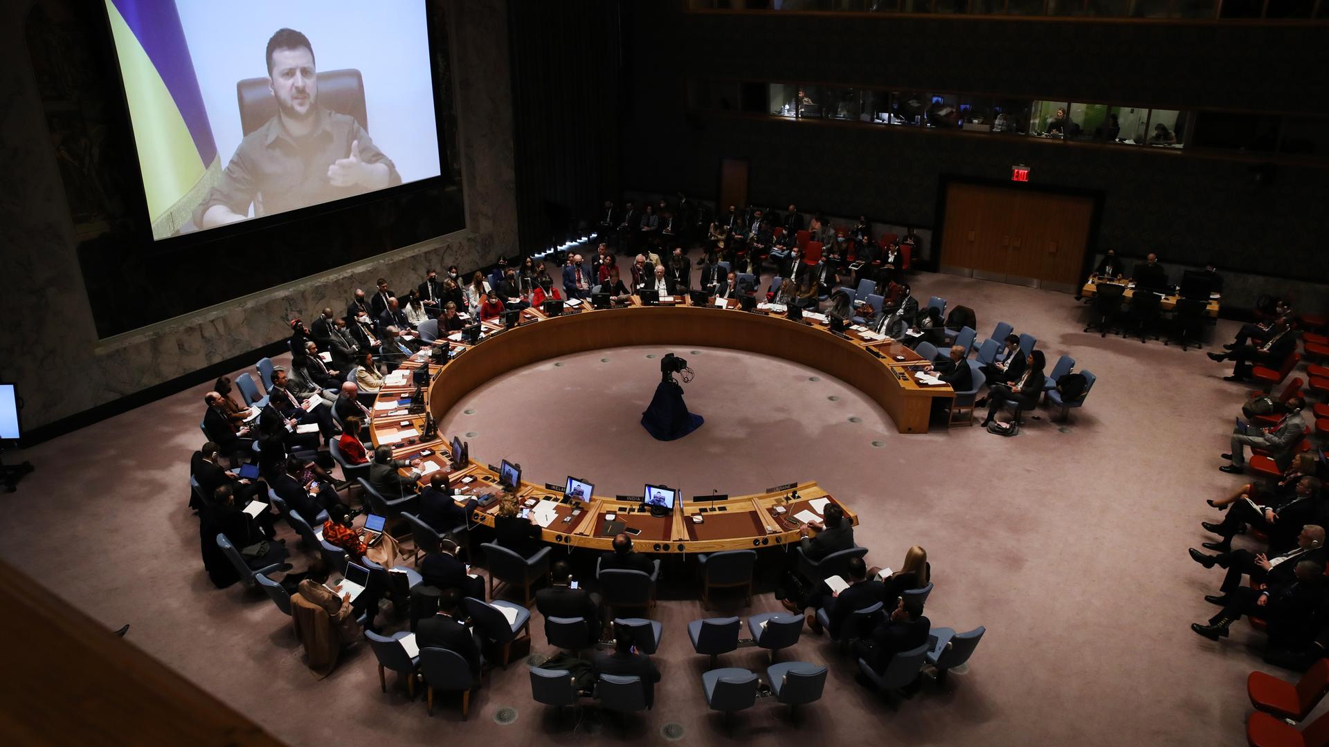 Auf einem Monitor ist der ukrainische Präsident Wolodymyr Selenskyj zu sehen. Im Raum der UN ein großer kreisrunder Tisch mit den UN Vertretern.