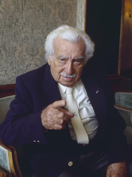 Jorge Amado sitzt in einer Lobby auf einem Sessel und deutet mit ernstem Blick in die Kamera. Jorge Amado sitzt in einer Lobby auf einem Sessel und deutet mit ernstem Blick in die Kamera.