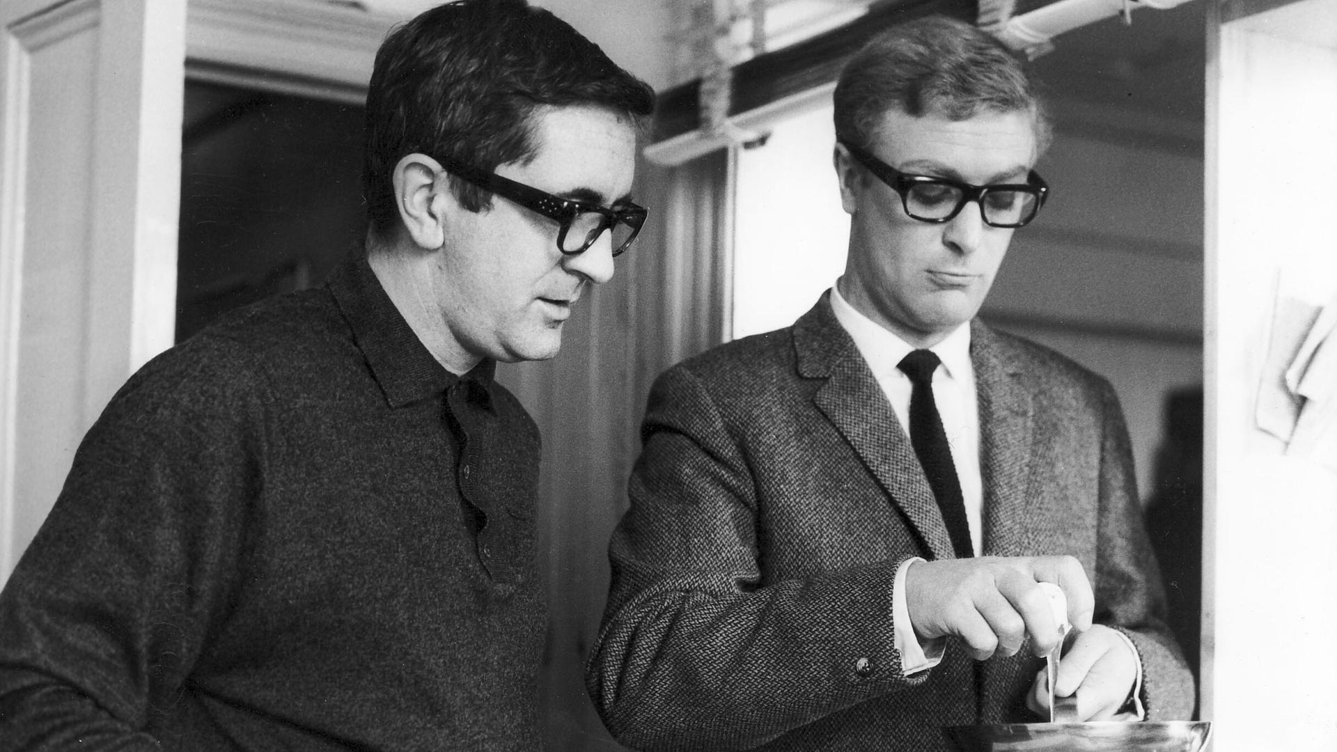 Der Schriftsteller Len Deighton und der Schauspieler Michael Caine im Jahr 1965, offenbar beim Aufschlagen eines Eis in eine Pfanne