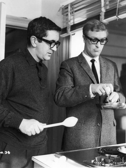 Der Schriftsteller Len Deighton und der Schauspieler Michael Caine im Jahr 1965, offenbar beim Aufschlagen eines Eis in eine Pfanne
