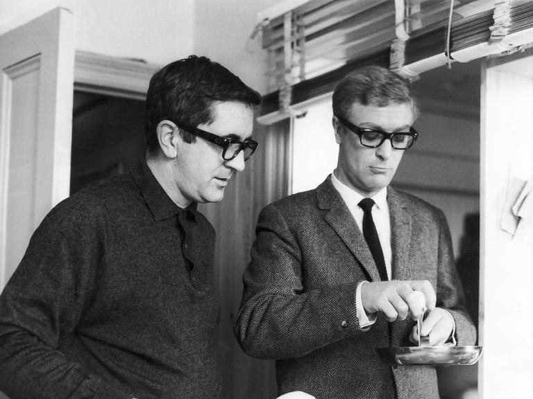 Der Schriftsteller Len Deighton und der Schauspieler Michael Caine im Jahr 1965, offenbar beim Aufschlagen eines Eis in eine Pfanne