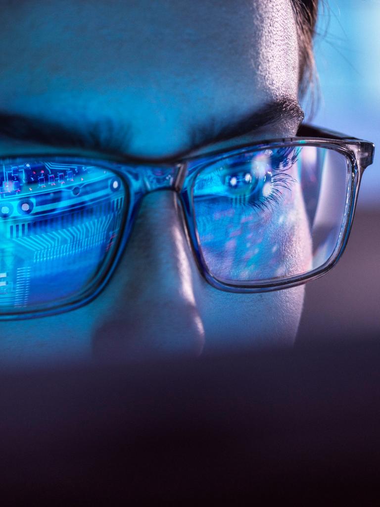 Nahaufnahme eines Mannes in dessen Brillengäsern sich Datenleitungen bzw. ein Computerchip spiegeln.