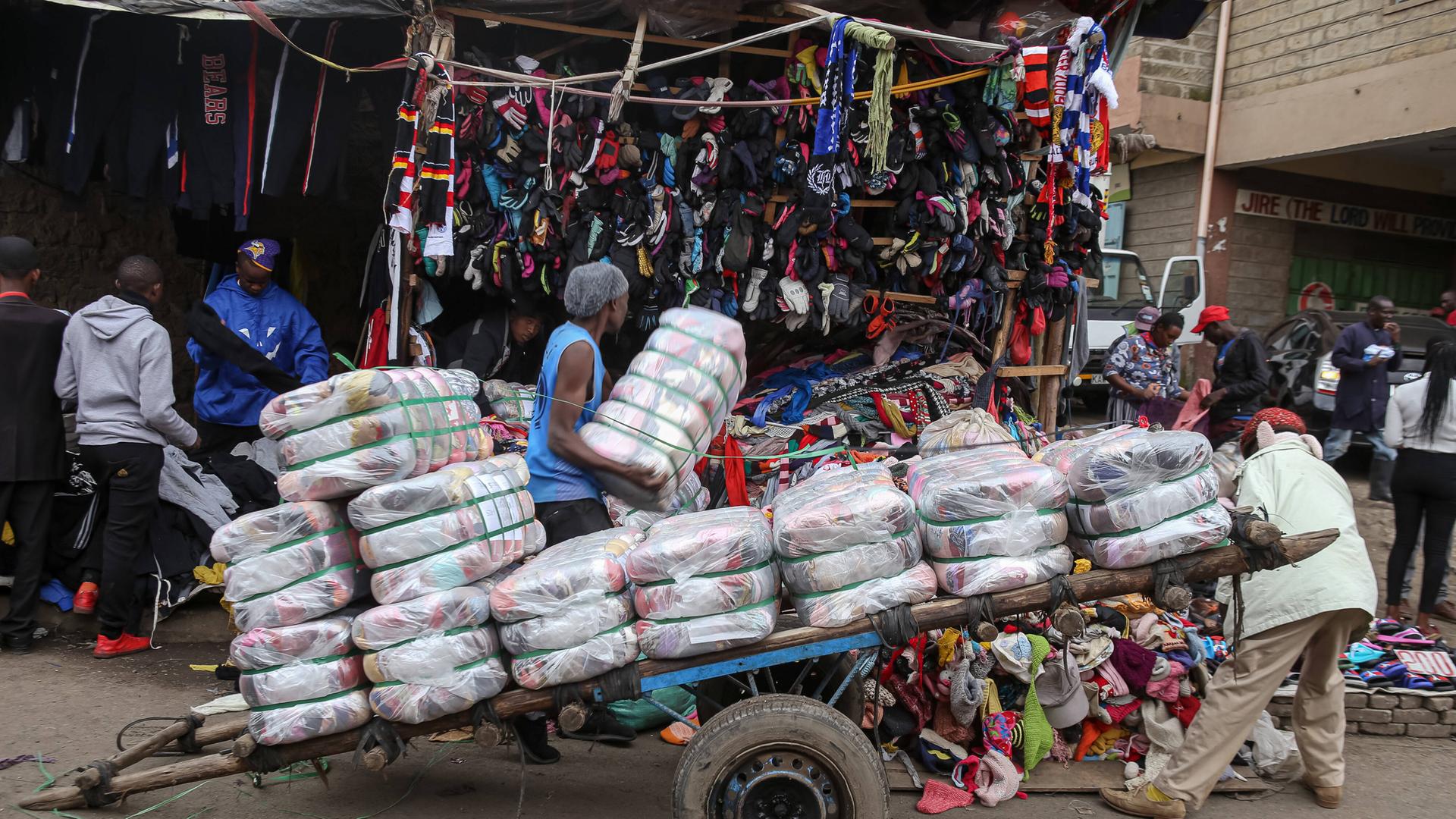 Mann schiebt Wagen mit in Bündel gepressten Altkleiderklamotten über den Gikomba Market in Nairobi, Kenia.