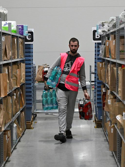Automatisiertes Distributionszentrum des tschechischen Online-Lebensmittelhändlers Rohlik in Chrastany bei Prag. Ein Mitarbeiter in Warnweste läuft mit Lebensmitteln durch Regalreihen mit vollgepackten Paketen und Taschen