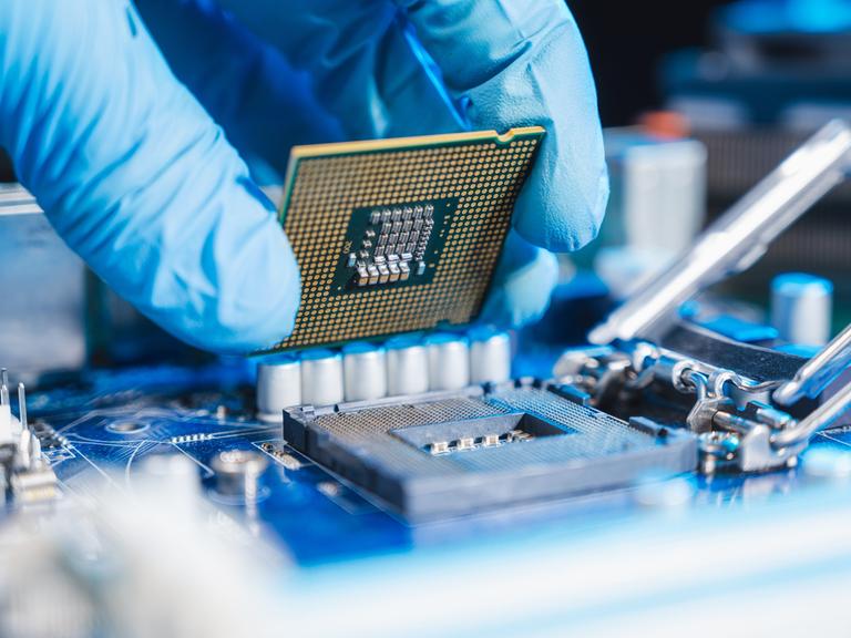 Halbleiter-Produktion: Nahaufnahme einer Hand, die eine CPU (Central processing unit) einsetzt.