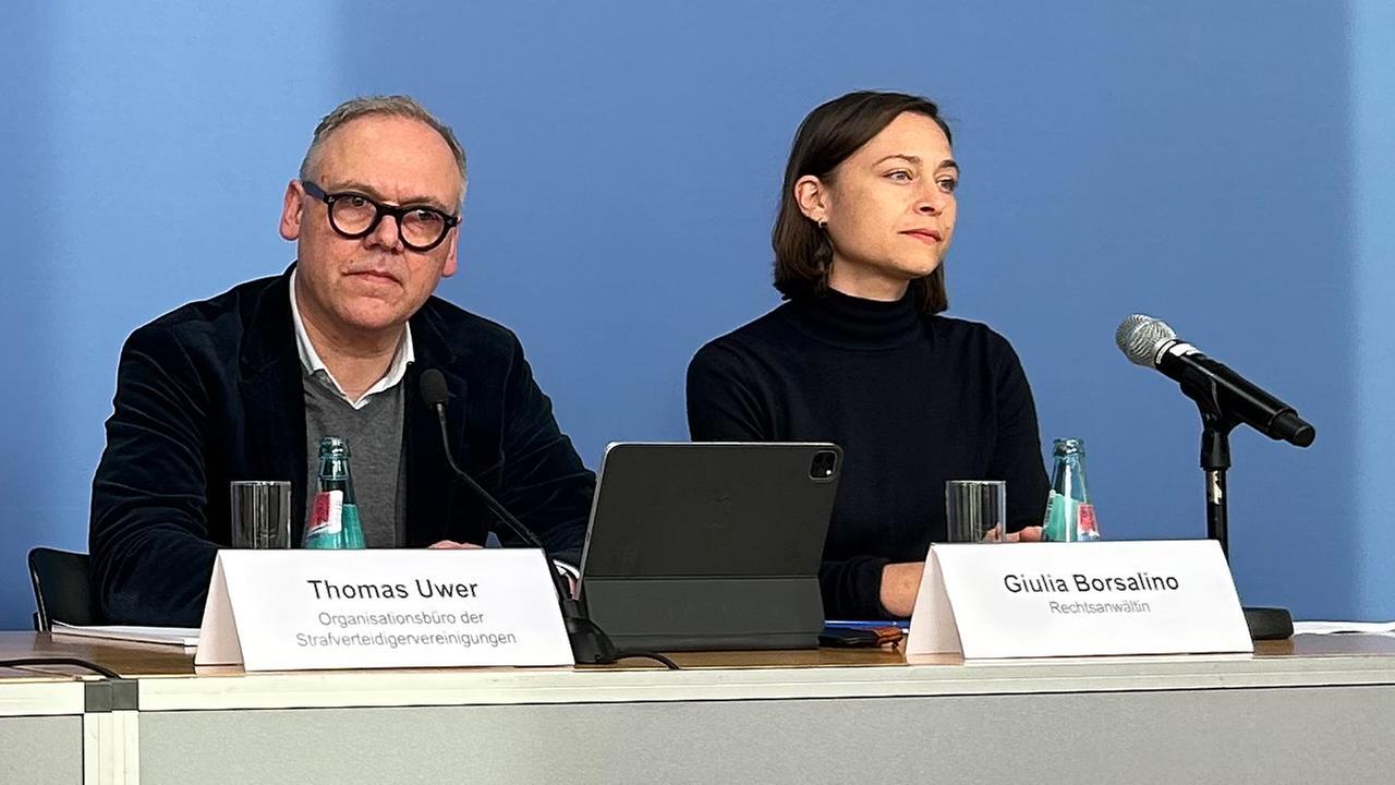 Die Leipziger Rechtsanwältin Giulia Borsalino und Thomas Uwer vom Organisationsbüro der Strafverteidigervereinigungen sitzen in der Bundespressekonferenz und sprechen zu Journalisten.