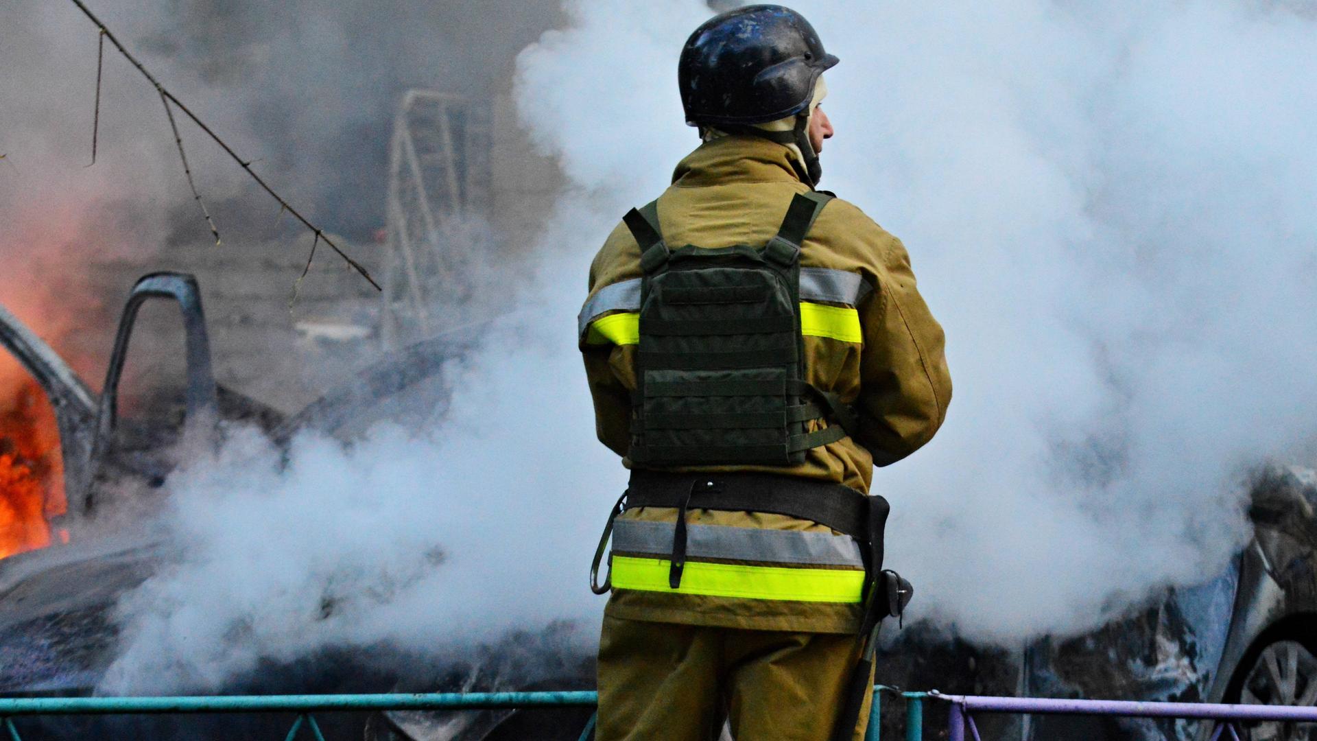 Ein Feuerwehrmann steht vor brennenden Trümmern und löscht.
