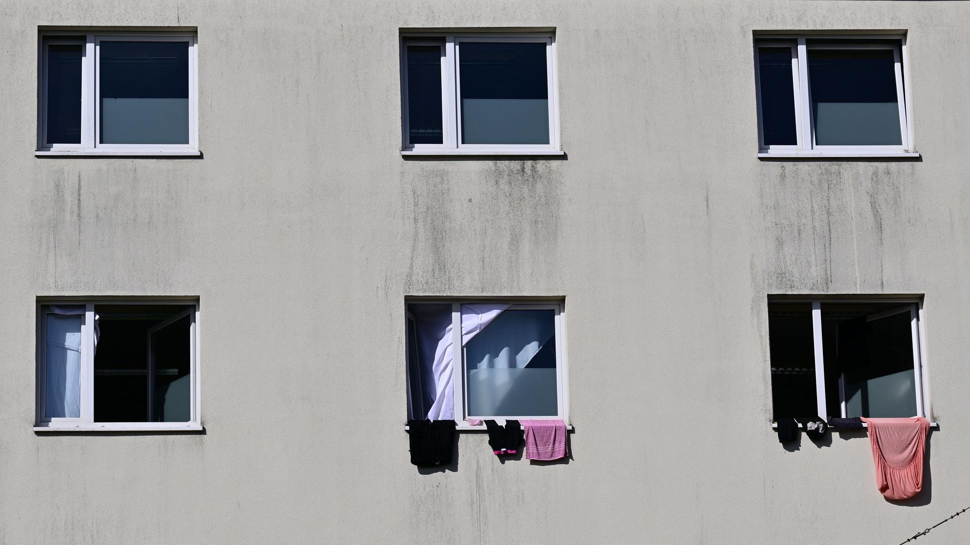 Die Landeserstaufnahmeeinrichtung auf dem Suhler Friedberg. Eine triste graue Häuserfassade mit Fenstern, aus denen einige Kleidungsstücke heraushängen. 