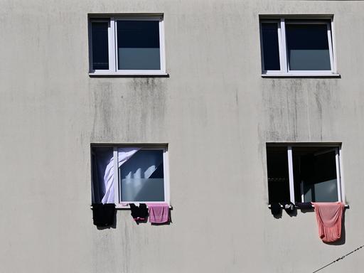Die Landeserstaufnahmeeinrichtung auf dem Suhler Friedberg. Eine triste graue Häuserfassade mit Fenstern, aus denen einige Kleidungsstücke heraushängen. 