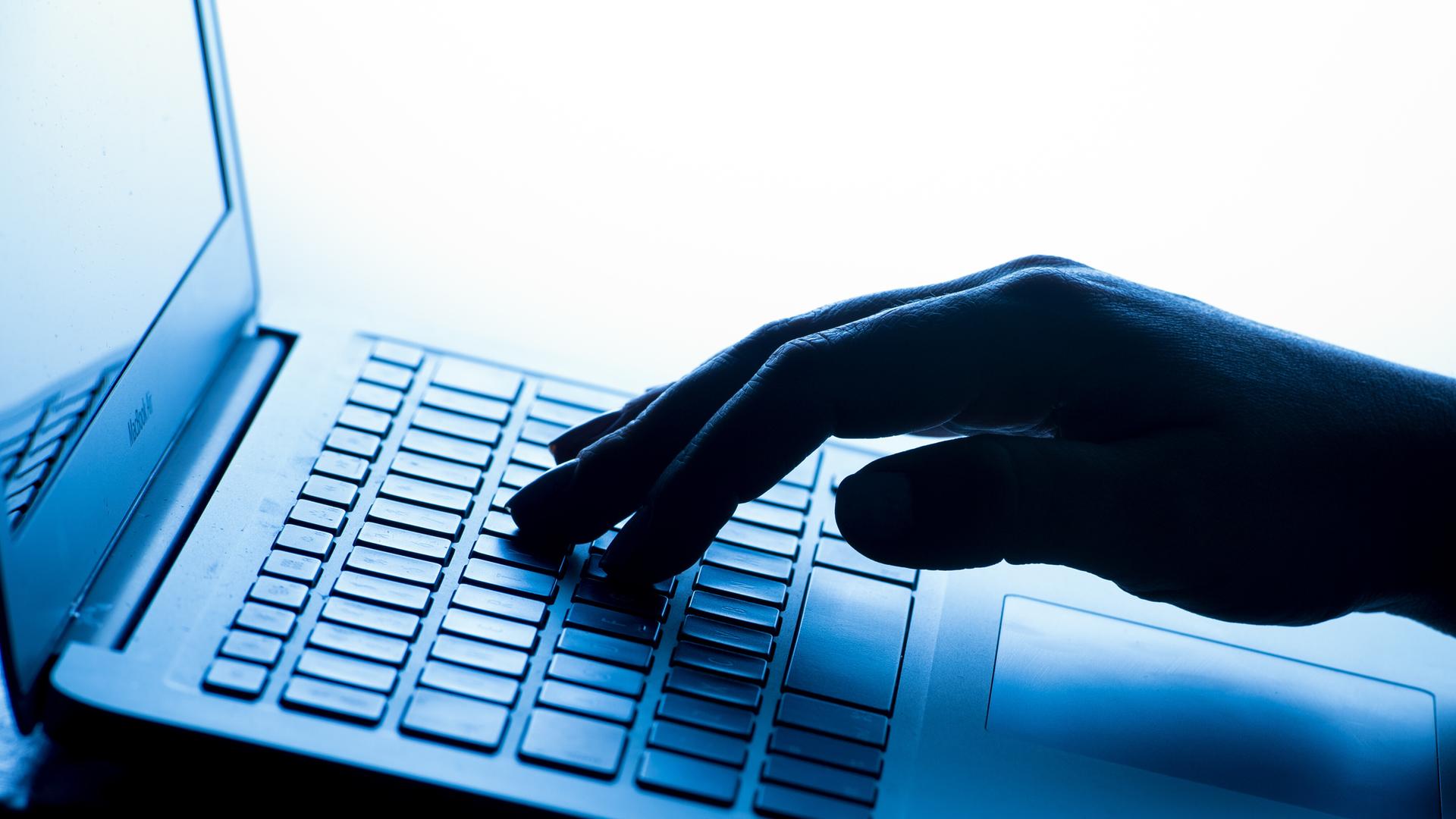 Eine Frauenhand in Nahaufnahme tippt auf einem Laptop, die Szene wirkt durch blaues Licht kühl und technisch.