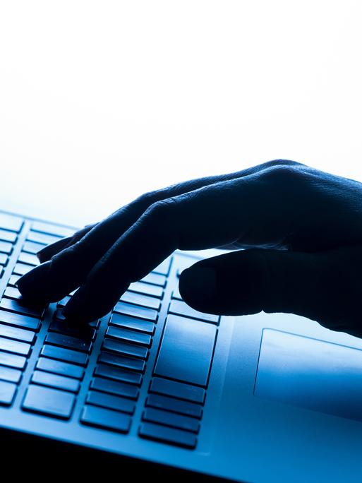Eine Frauenhand in Nahaufnahme tippt auf einem Laptop, die Szene wirkt durch blaues Licht kühl und technisch.