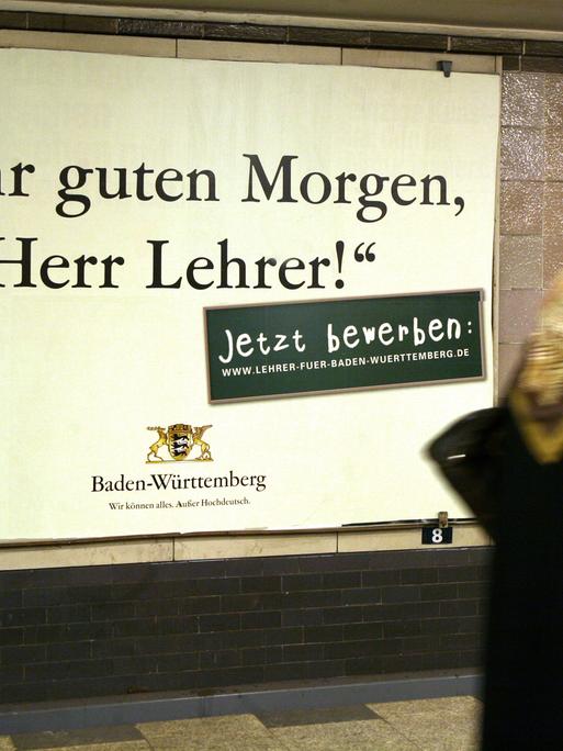 Eine Frau läuft in einem Berliner U-Bahnhof an einem Werbeplakat vorbei, auf dem Baden-Württemberg für den Lehrerberuf wirbt. Darauf steht in einer altmodischen Schrift der Satz: "Sehr guten Morgen, Herr Lehrer." 