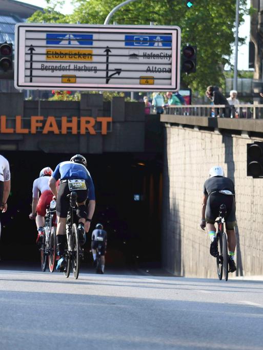 Teilnehmer des Ironman-Rennens in Hamburg fahren auf ihren Fahrrädern an der Kunsthalle in einen Tunnel. 