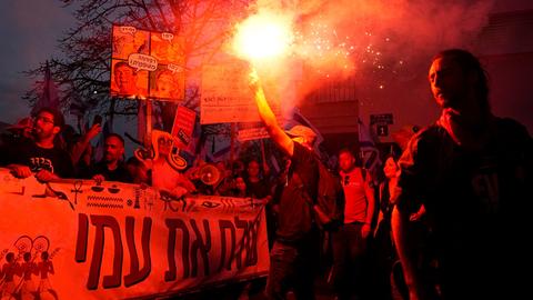 Menschen protestieren in Tel Aviv gegen die Justizpläne der Regierung. Es brennen Fackeln und andere Leuchtmittel.
