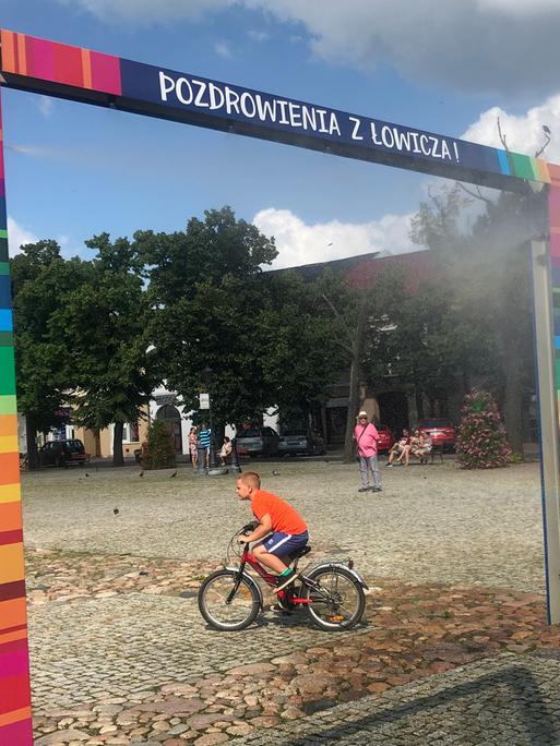 Es ist nicht, wie es scheint. Die bunten Farben auf dem Marktplatz von Łowicz nördöstlich von Łódź verweisen auf traditionelle Volkskunst – nicht auf die LGBT-Flagge. Zu sehen: Ein Spielplatz in Lowicz, Polen. Ein Kind auf einem Fahrrad durchquert das Bild. 