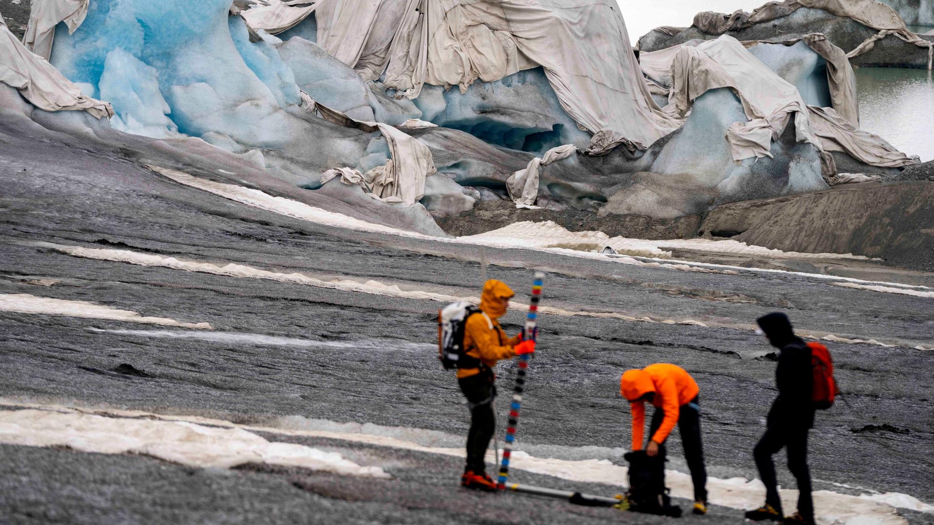 Drei Glaziologen der Hochschule ETH: Zwei von ihnen tragen hellorange, leuchtende Kleidung. Sie beginnen ihre Arbeiten vor dem Rhonegletscher bei Goms in der Schweiz