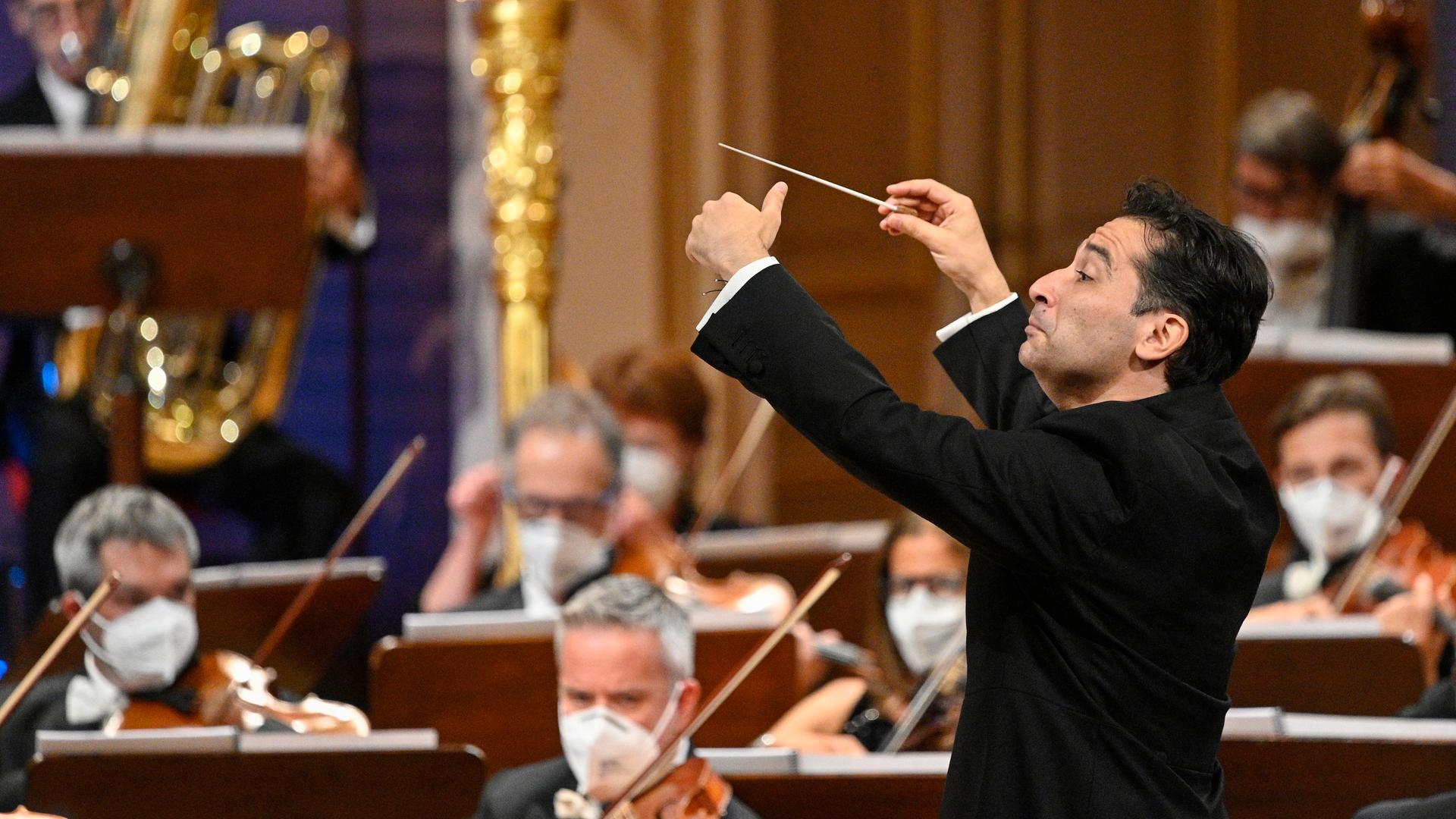 Ein Dirigent erhebt seinen Taktstock vor einem Orchester. Ein Dirigent erhebt seinen Taktstock vor einem Orchester.