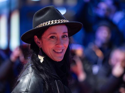 Esther Perbandt trägt einen schwarzen Hut, eine schwarze Lederjacke und schaut lachend in die Kamera.