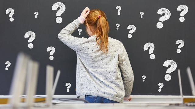 Kind steht in der Grundschule vor einer Tafel mit vielen Fragezeichen