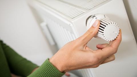 Eine Hand dreht am Temperaturregler einer Heizung. 