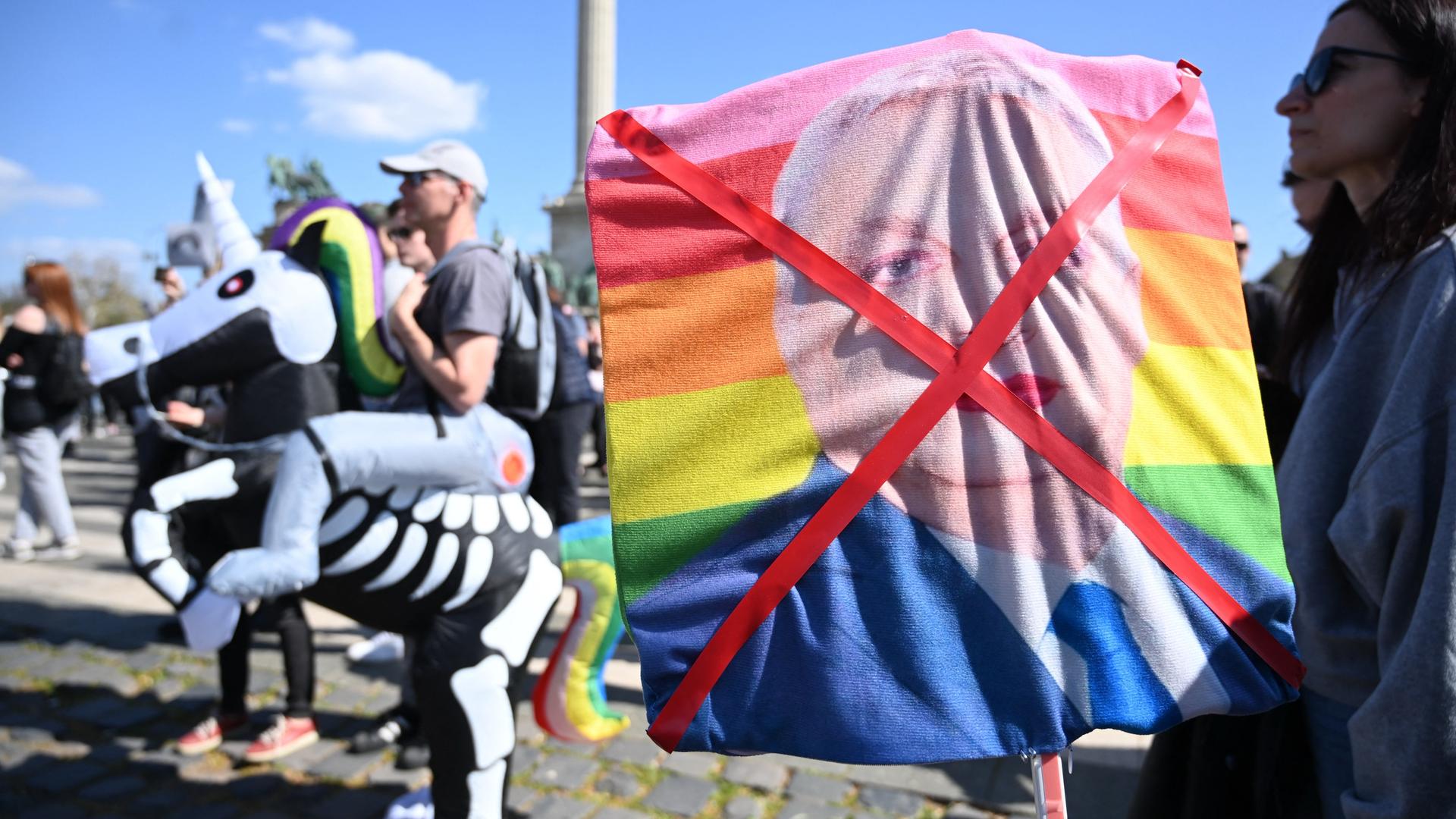 Demonstrantin hält durchgestrichenes Bild mit geschminkten ungarischen Premierministers Viktor Orban auf einer Regenbogenfahne (12.4.2025)