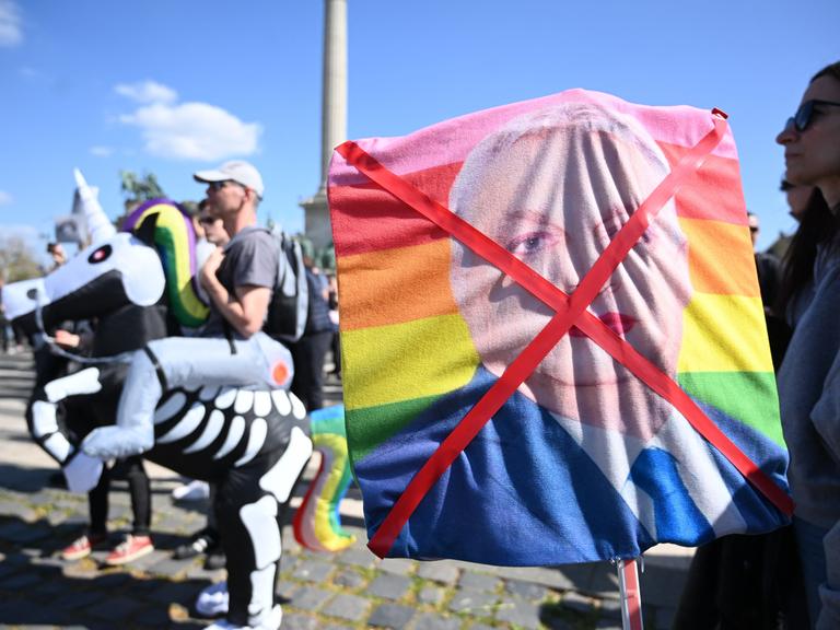 Demonstrantin hält durchgestrichenes Bild mit geschminkten ungarischen Premierministers Viktor Orban auf einer Regenbogenfahne (12.4.2025)