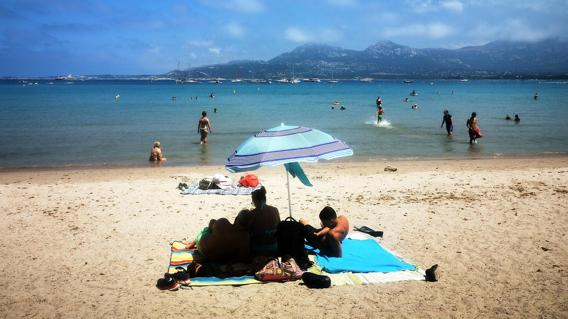Menschen liegen am Strand von Korsika unter Sonnenschirmen. Menschen liegen am Strand von Korsika unter Sonnenschirmen.