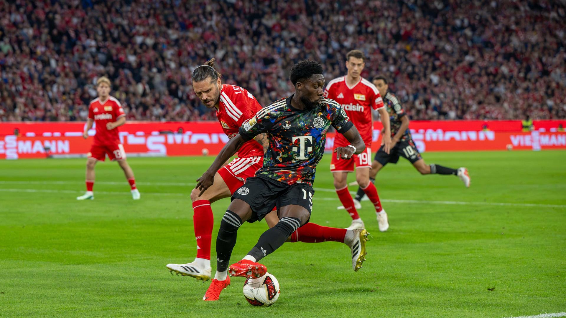 Bayern München spielt gegen Union Berlin. Spieler beider Mannschaften kämpfen um den Ball.