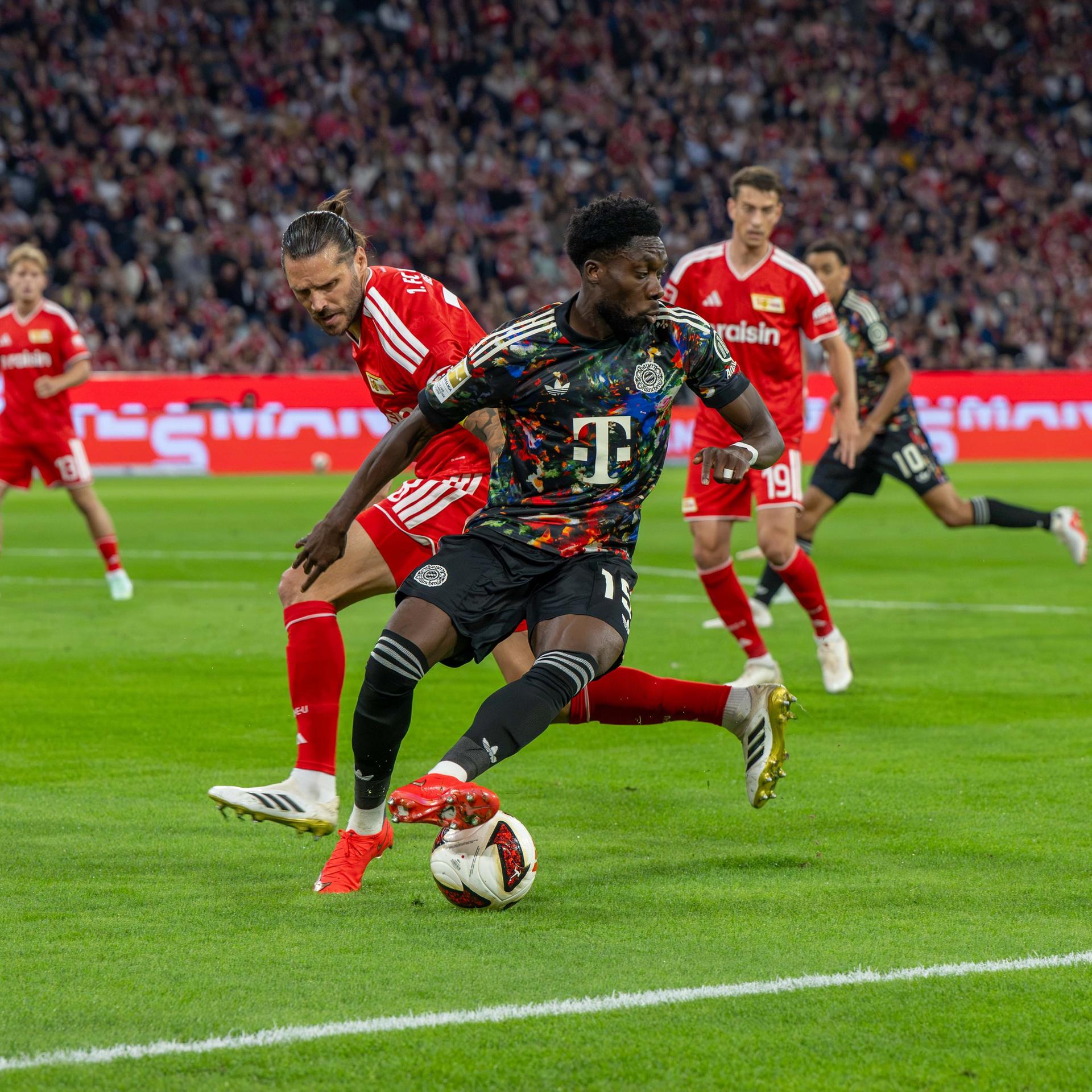 Bayern München spielt gegen Union Berlin. Spieler beider Mannschaften kämpfen um den Ball.