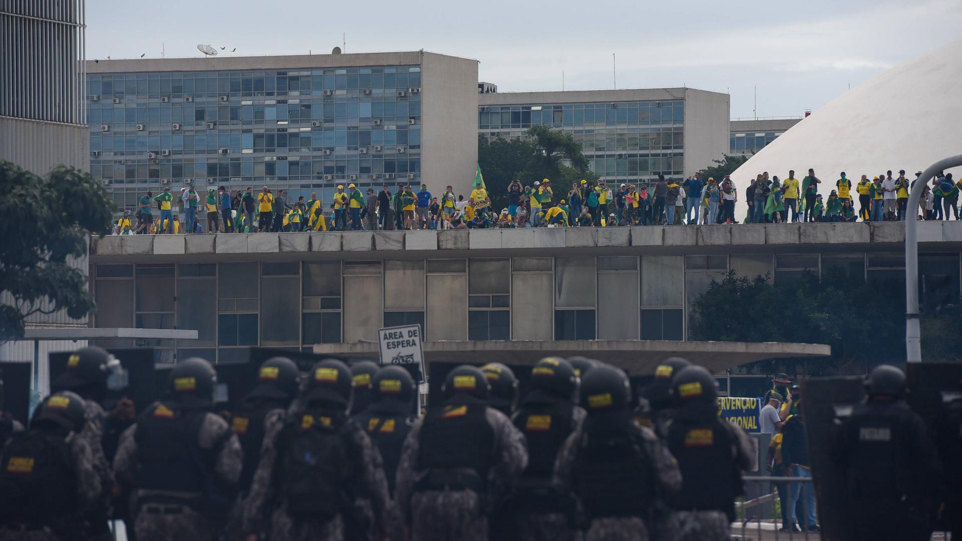 Anhänger des Ex-Präsidenten Jair Bolsonaro stürmen mehrere Regierungsgebäude in Brasilia, im Vordergrund rücken Polizisten in schwerer Ausrüstung an. Anhänger des Ex-Präsidenten Jair Bolsonaro stürmen mehrere Regierungsgebäude in Brasilia, im Vordergrund rücken Polizisten in schwerer Ausrüstung an.