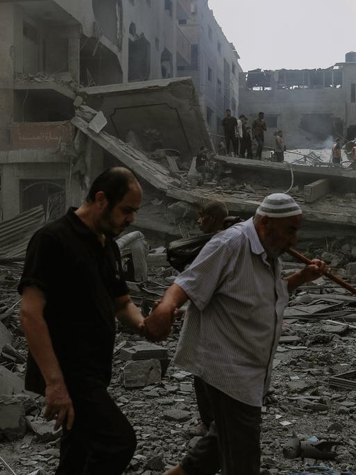 Ein alter Mann geht auf einen jungen Mann gestützt durch die Ruine eines Hauses nach einem Bombenangriff im Gazastreifen.