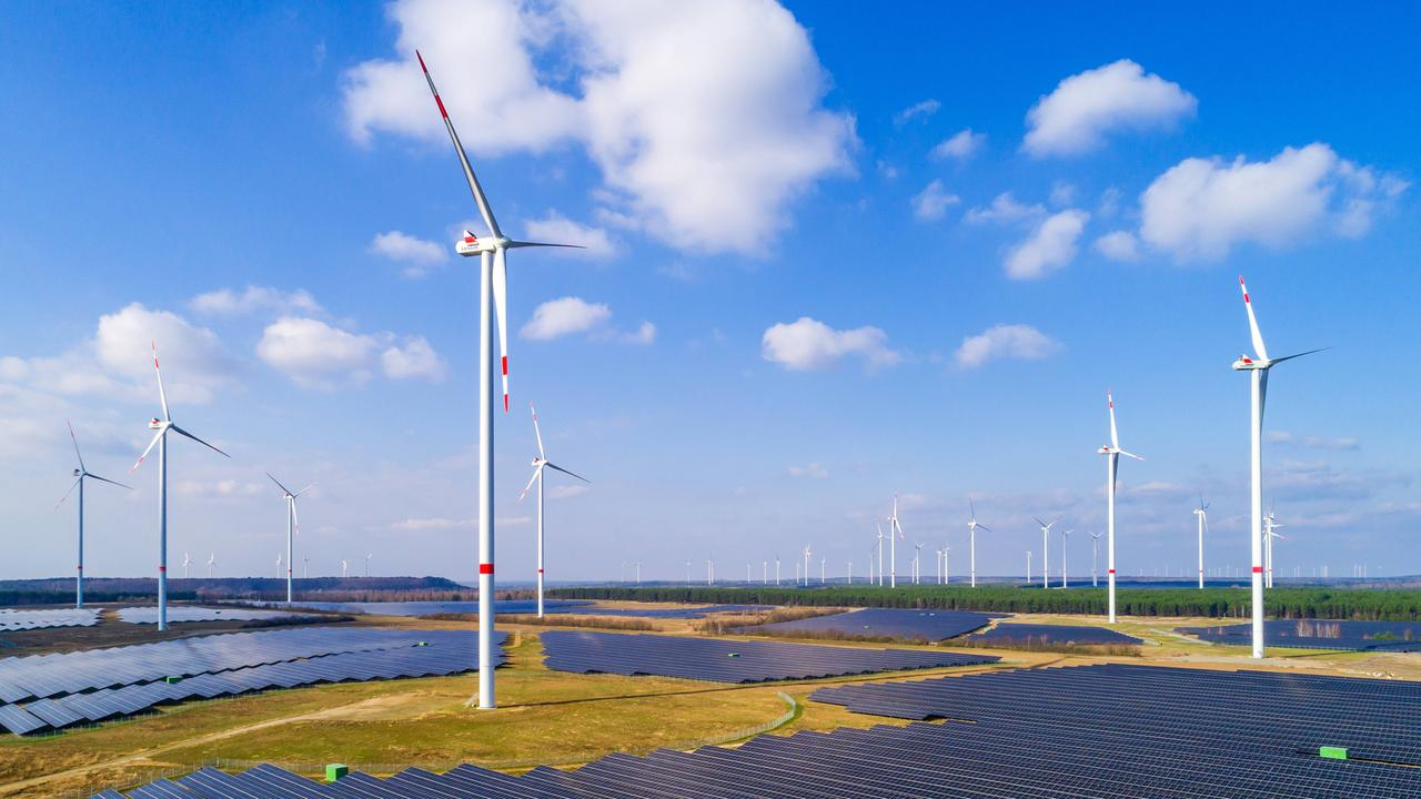 Windräder stehen auf freiem Feld vor den Panelen einer Solaranlage.
