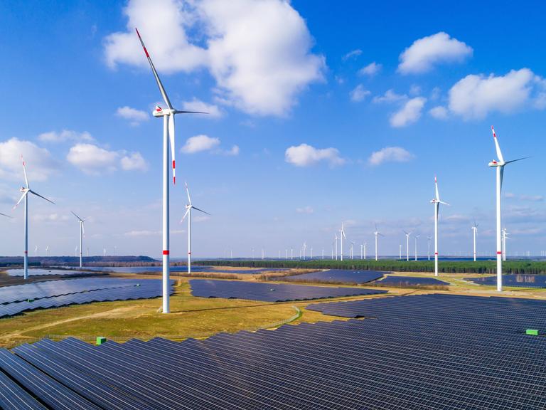 Windräder stehen auf freiem Feld vor den Panelen einer Solaranlage. Windräder stehen auf freiem Feld vor den Panelen einer Solaranlage.