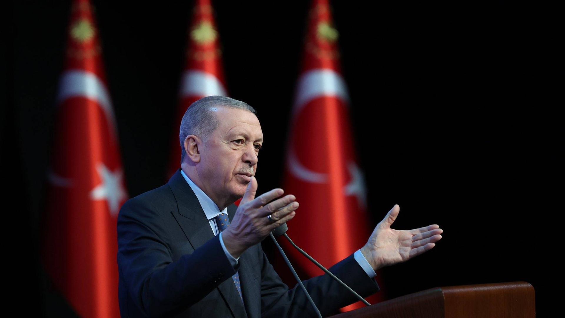 Recep Erdogan steht gestikulierend am Rednerpult; im Hintergrund stehen drei Türkeiflaggen.