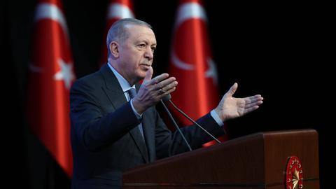 Recep Erdogan steht gestikulierend am Rednerpult; im Hintergrund stehen drei Türkeiflaggen.