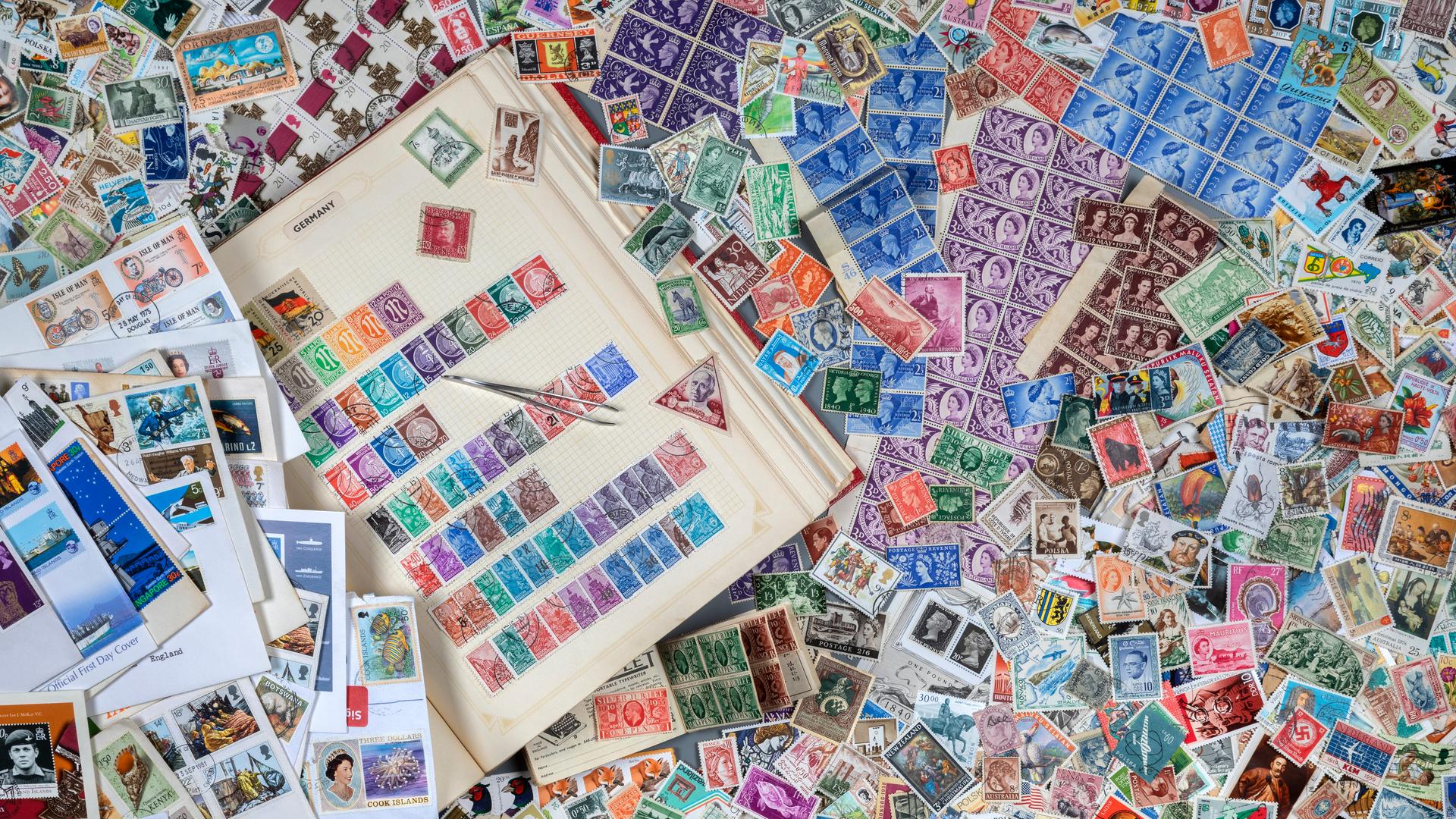 Ein Tisch, auf dem ein Buch mit Briefmarken zu sehen ist. Drumherum liegen hunderte von anderen Briefmarken herum. Ein Tisch, auf dem ein Buch mit Briefmarken zu sehen ist. Drumherum liegen hunderte von anderen Briefmarken herum.