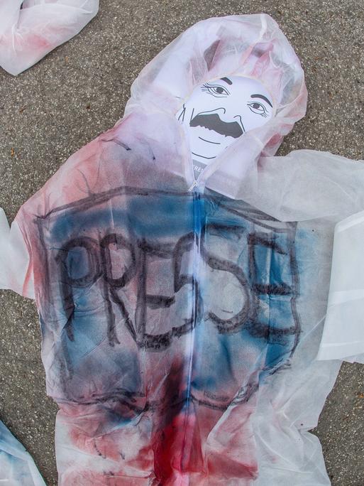 Eine männliche Figur mit der Aufschrift "Presse" auf der Brust liegt auf dem Boden.