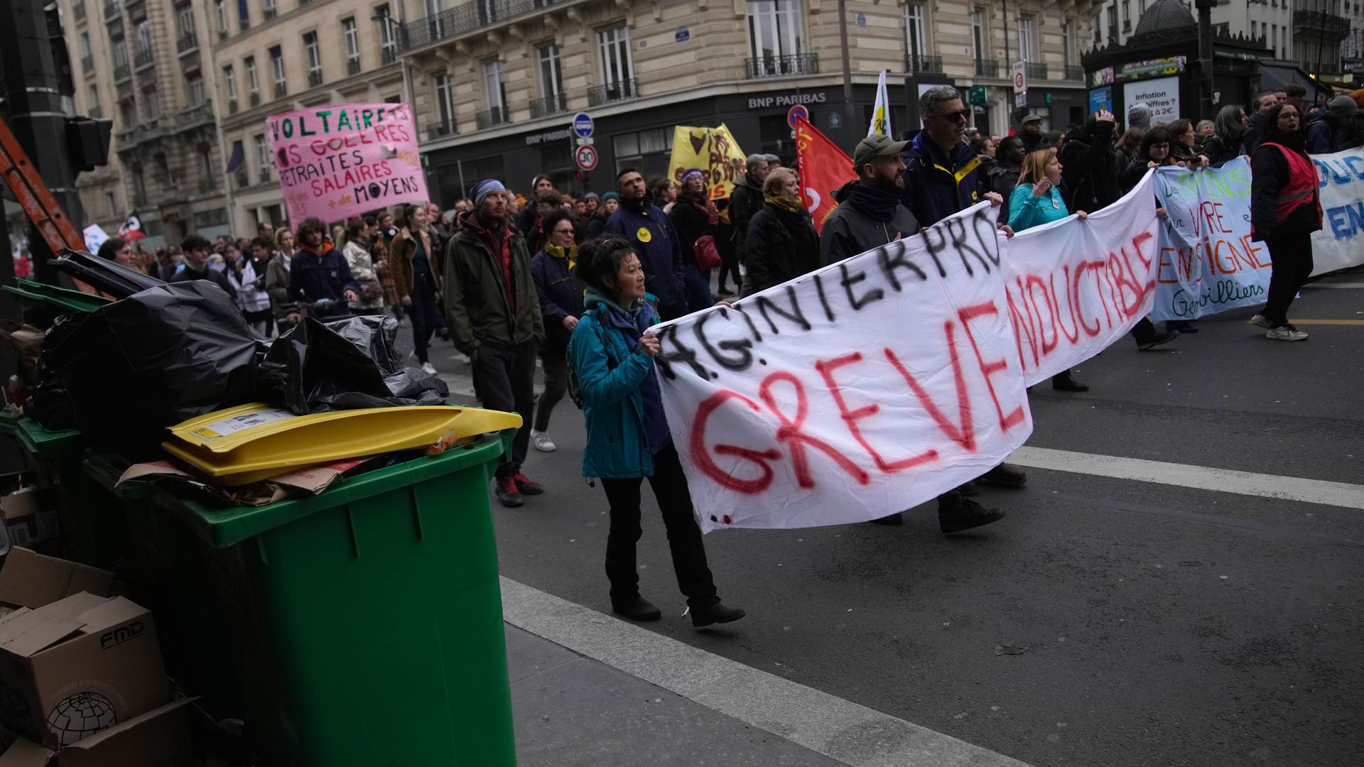 Studenten marschieren während einer Demonstration am Donnerstag, 9. März 2023, in Paris an nicht abgeholten Mülltonnen vorbei. Sie protestieren gegen die geplante Rentenreform.