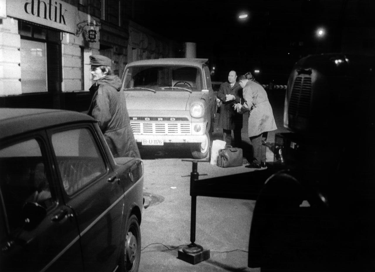 An einer nächtlichen Straße in Berlin im Dezember 1971 stehen Polizisten neben geparkten Autos.