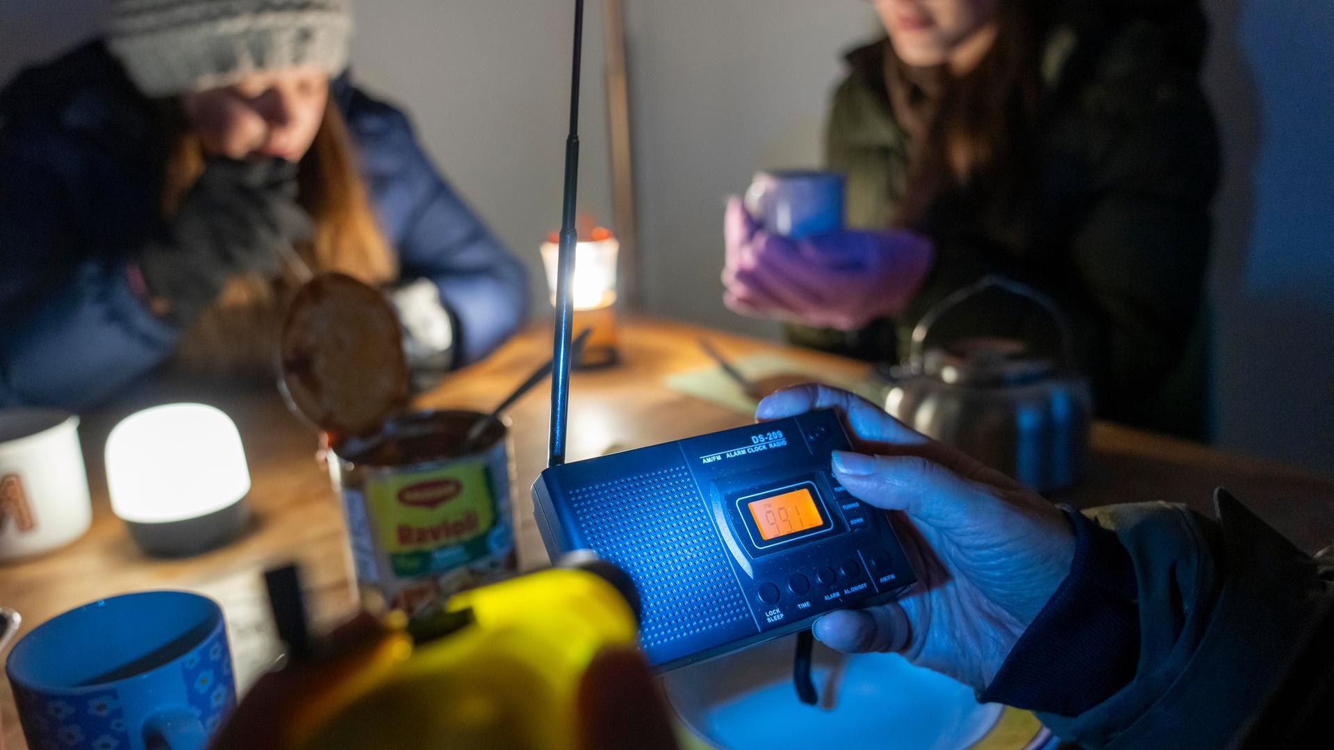 Symbolbild Katastrophe und Stromausfall: Menschen sitzen in warmer Kleidung beim Licht von Taschenlampen