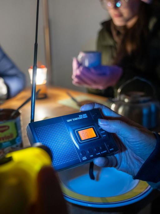 Symbolbild Katastrophe und Stromausfall: Menschen sitzen in warmer Kleidung beim Licht von Taschenlampen