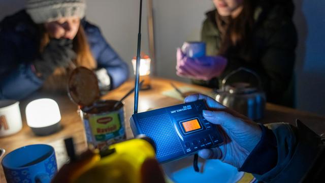 Symbolbild Katastrophe und Stromausfall: Menschen sitzen in warmer Kleidung beim Licht von Taschenlampen