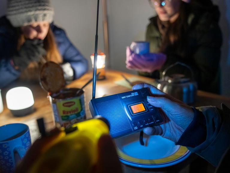 Symbolbild Katastrophe und Stromausfall: Menschen sitzen in warmer Kleidung beim Licht von Taschenlampen