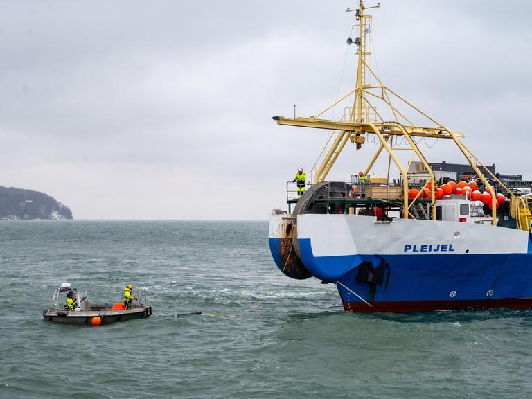 Das Kabelverlegeschiff „Pleijel“ liegt auf der Ostsee vor Rügen. Vor ihm ein bemanntes Schlauchboot - zwischen den Booten hängt ein gelbes Kabel, das Unterseekabel.