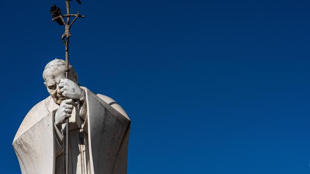 Statue von Papst Johannes Paul II. vor blauem Himmel. Die Statue zeigt den Papst in demütiger Haltung