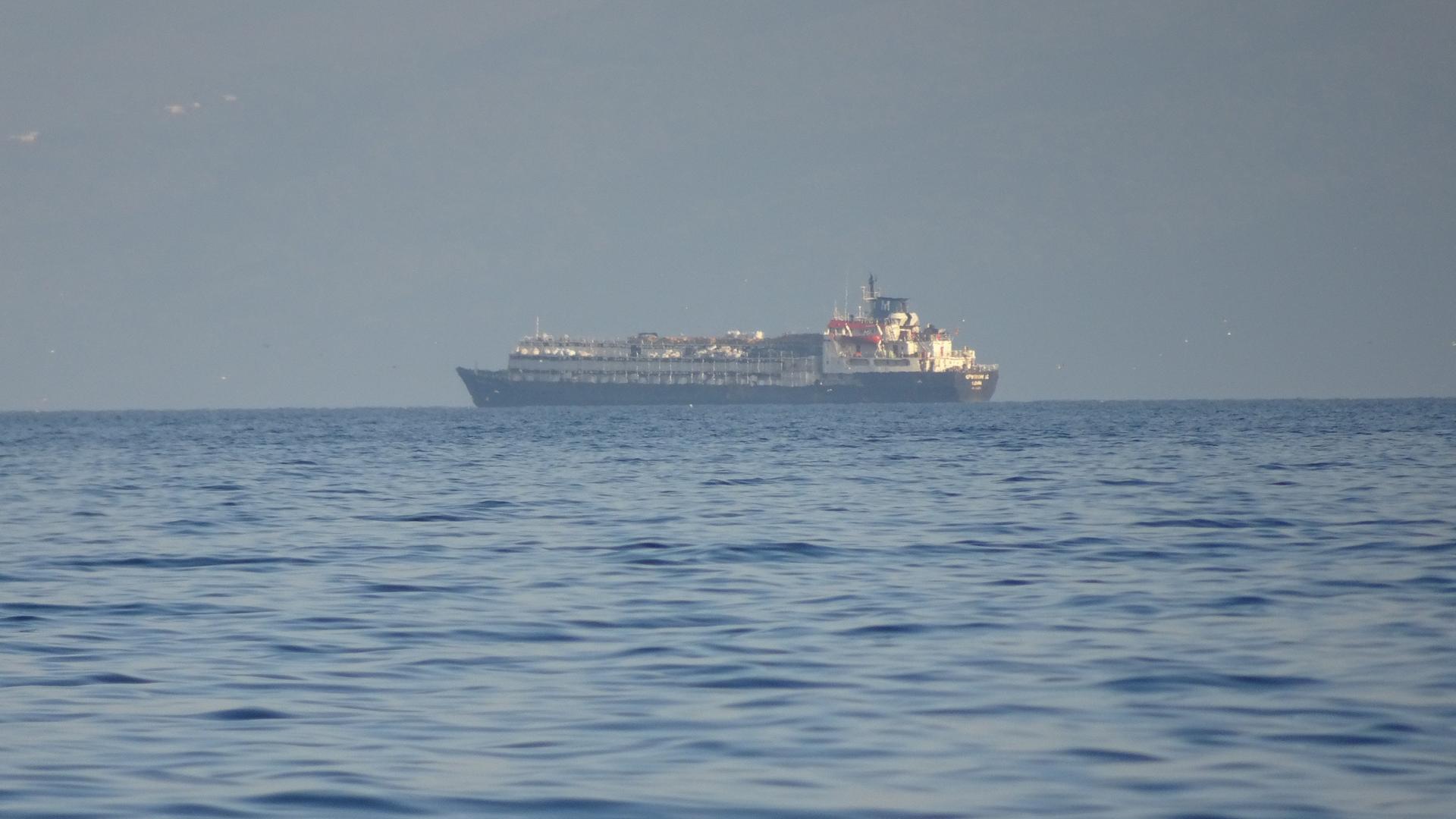 Blick aus großer Entfernung: Das Schiff ankert am Horizont auf dem blauen Meer.