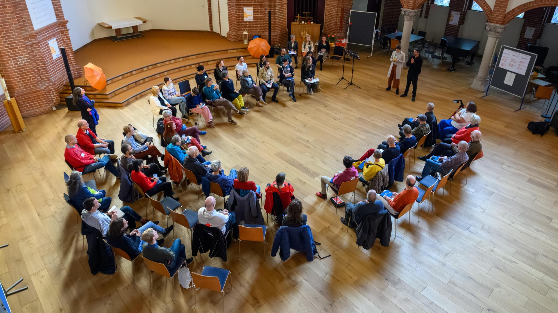 Etwa 50 Menschen sitzen in einem Halbkreis zusammen in einer Kirche.